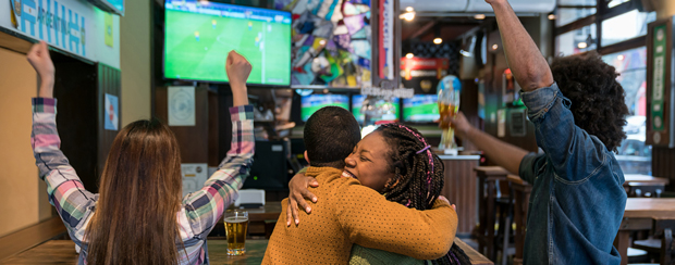 Customers at a bar/restaurant cheering while watching sporting event on TV